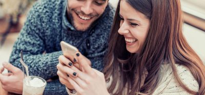 a man and woman sitting at a table looking at a cell phone.